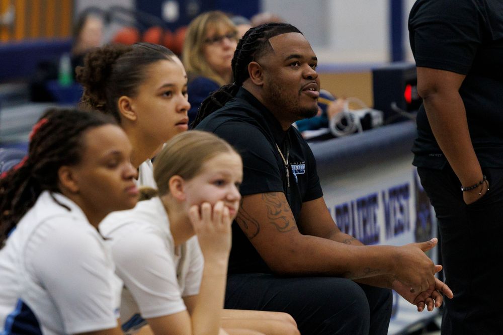 Team members and staff watching intently from sidelines during basketball game.