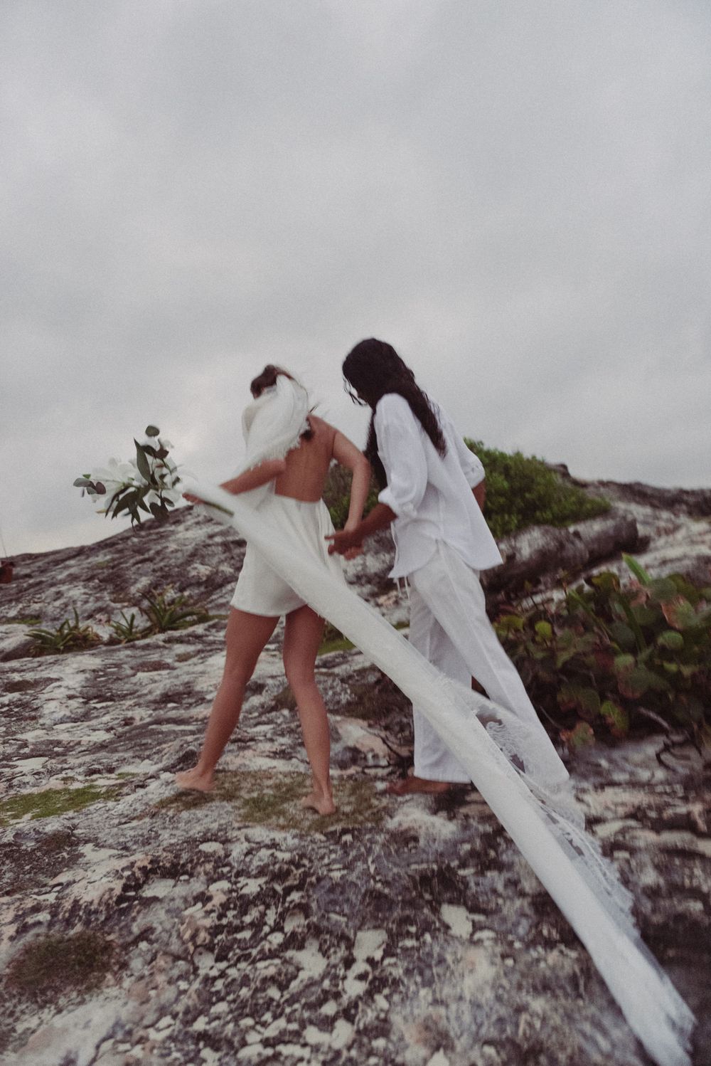 A bride and groom are walking together up a cliff on the beach in Tulum, Mexico.