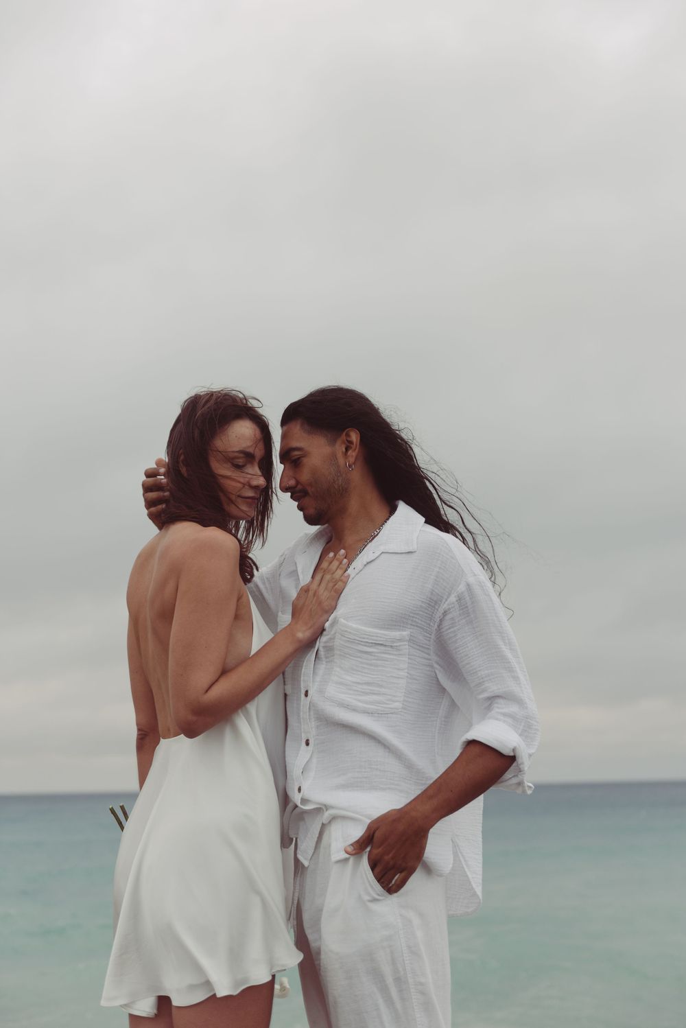 A bride and groom are embracing with the ocean behind them.