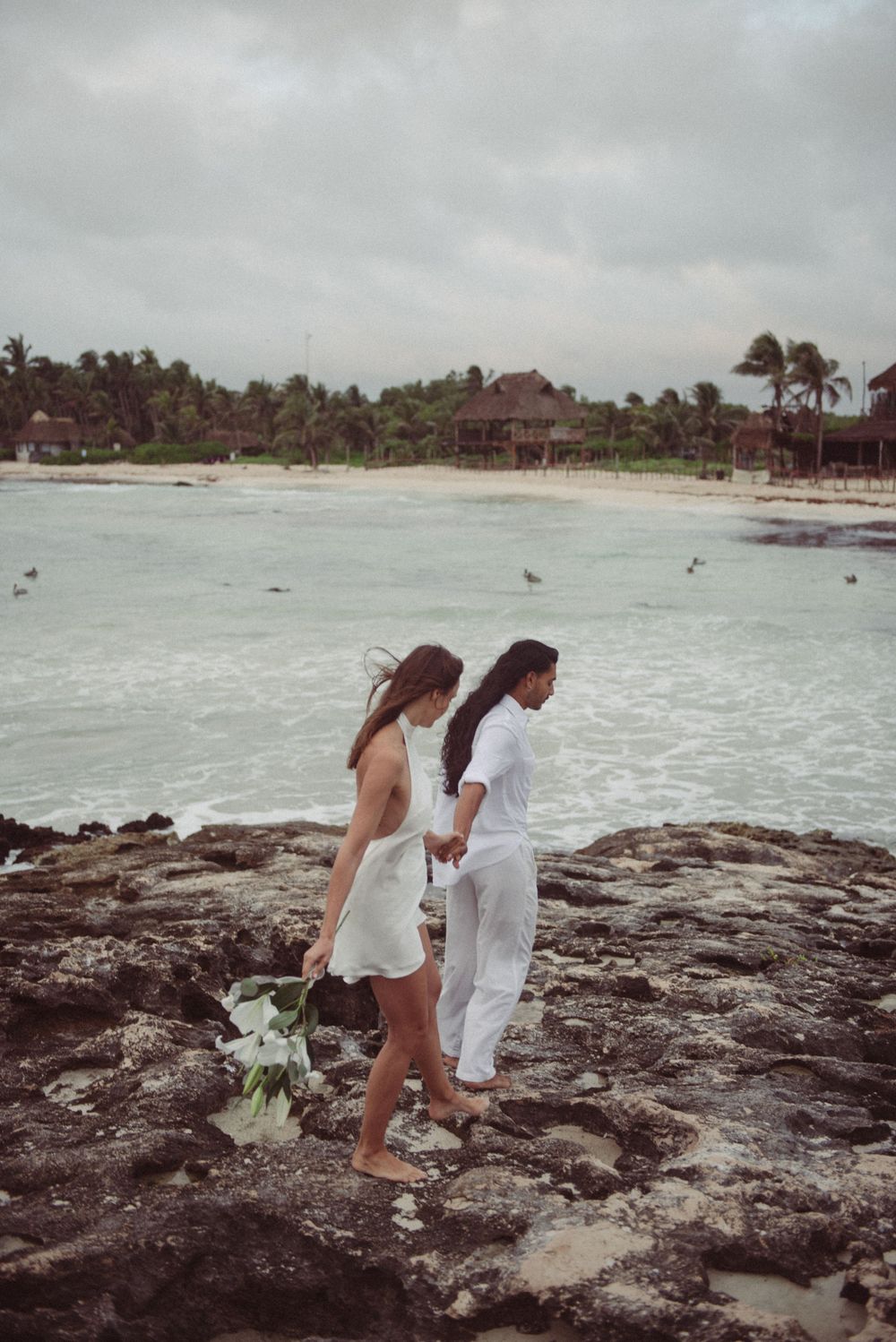 A bride and groom walking together on the beach in Tulum, Mexico.