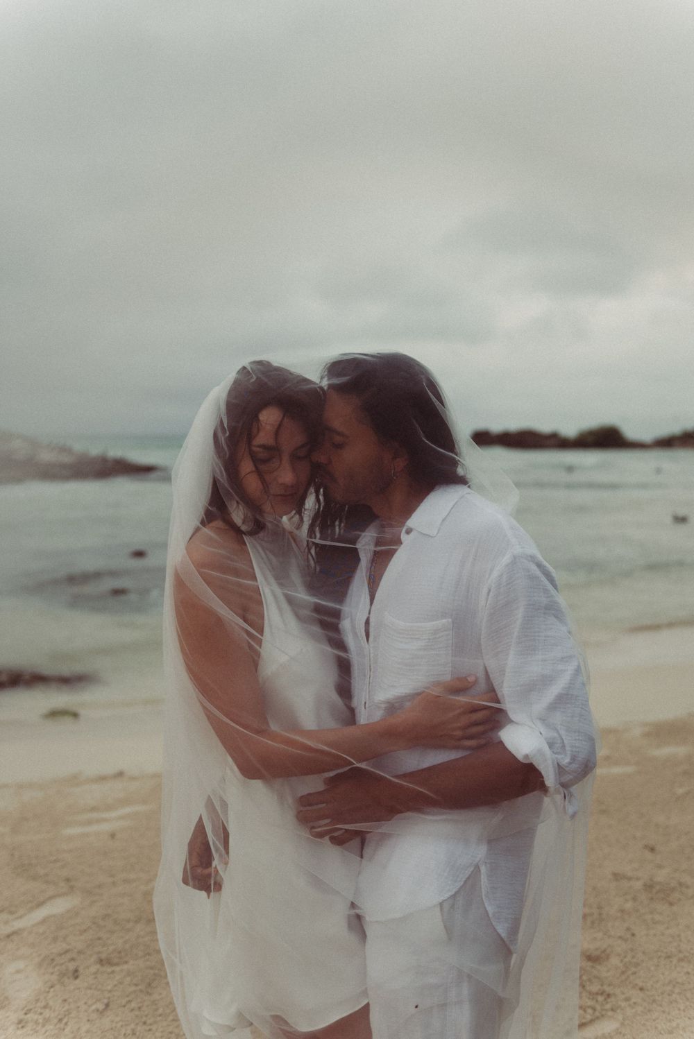 Romantic elopement featuring the couple embracing underneath the bride's veil on the beach in Tulum, Mexico.