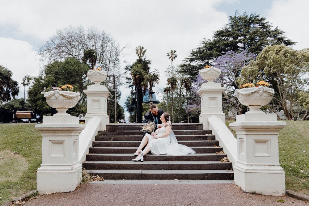 Elegant couple sits on grand outdoor stone staircase, captured by Apertured Media Auckland Wedding Photographer.