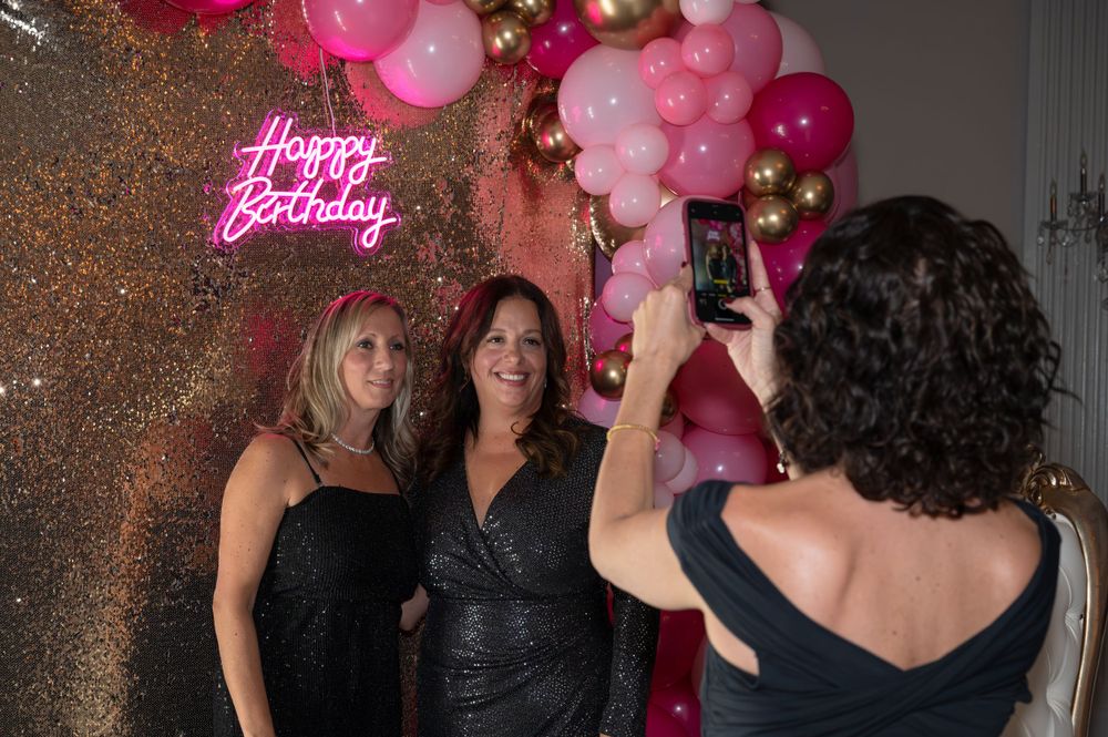 Pink and red balloons decorate a celebration with sparkly background and neon birthday sign.