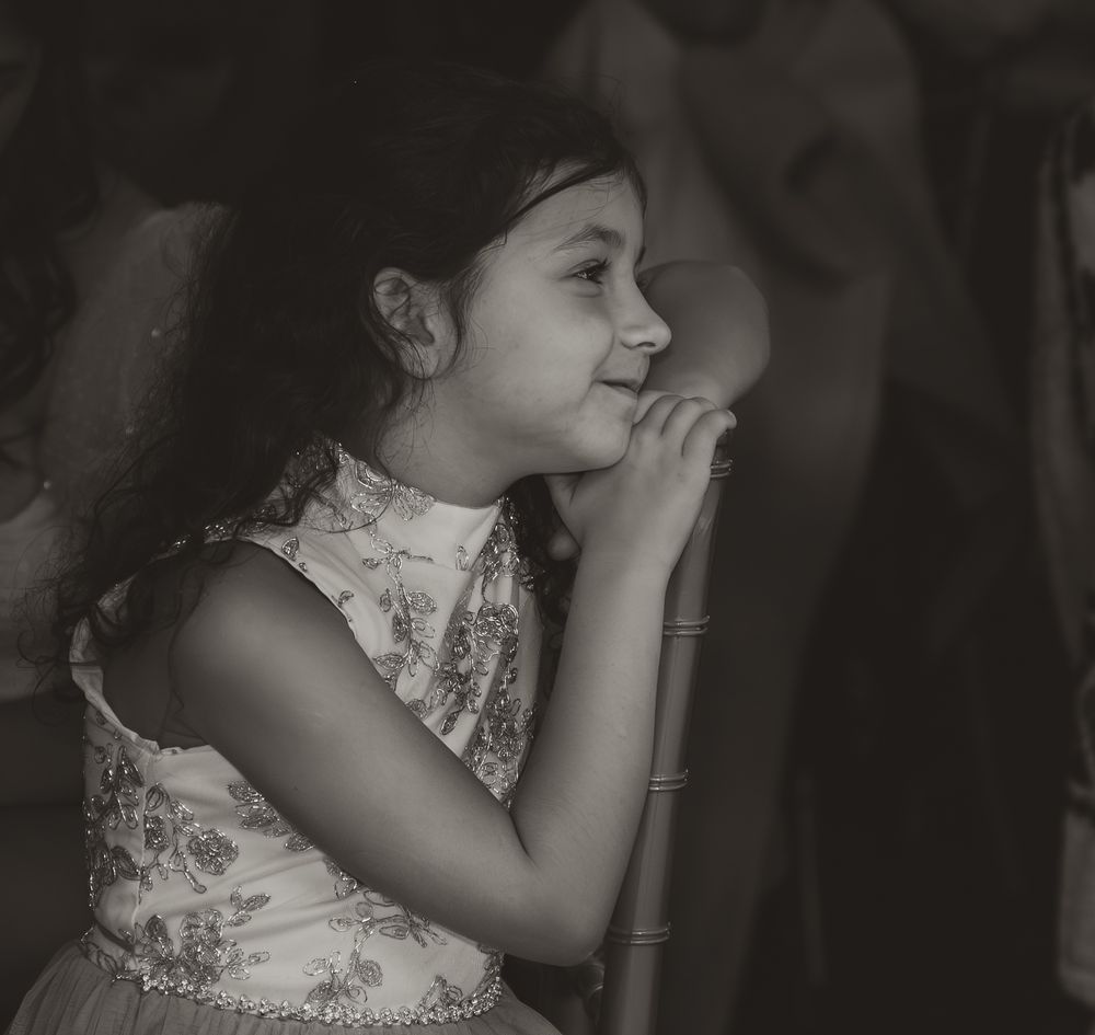 Black and white portrait of someone in an ornate dress looking down pensively.
