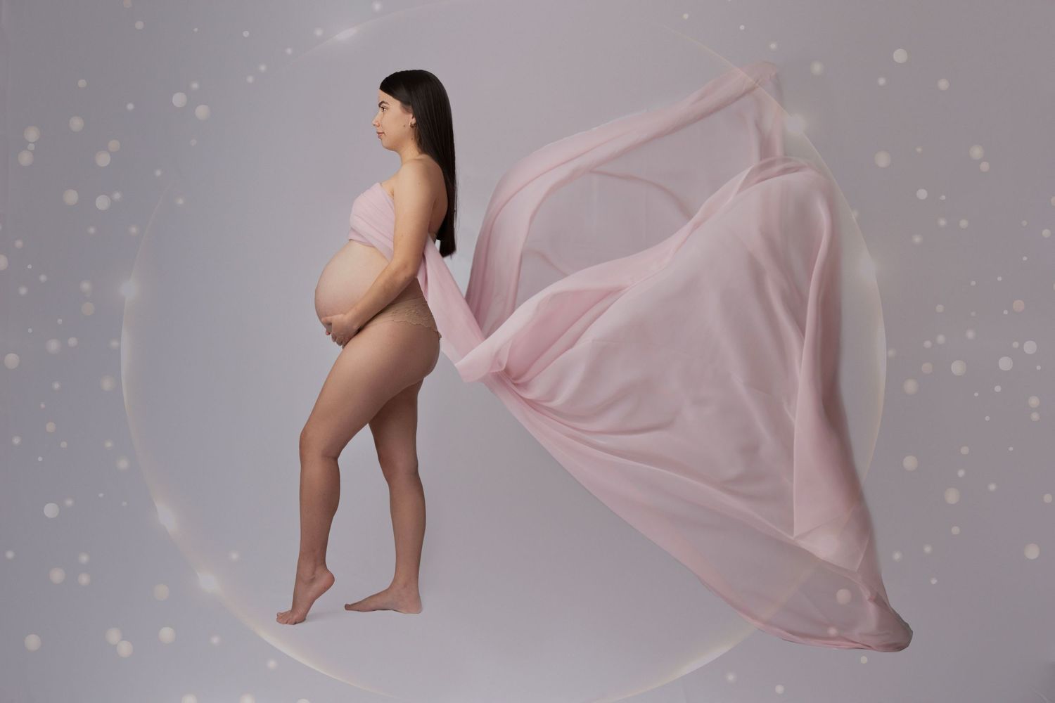 Pregnant woman posing elegantly with flowing pink fabric during maternity photoshoot.