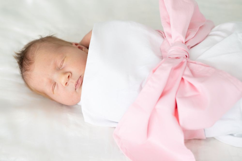 Sleeping newborn wrapped in white with large pink bow.