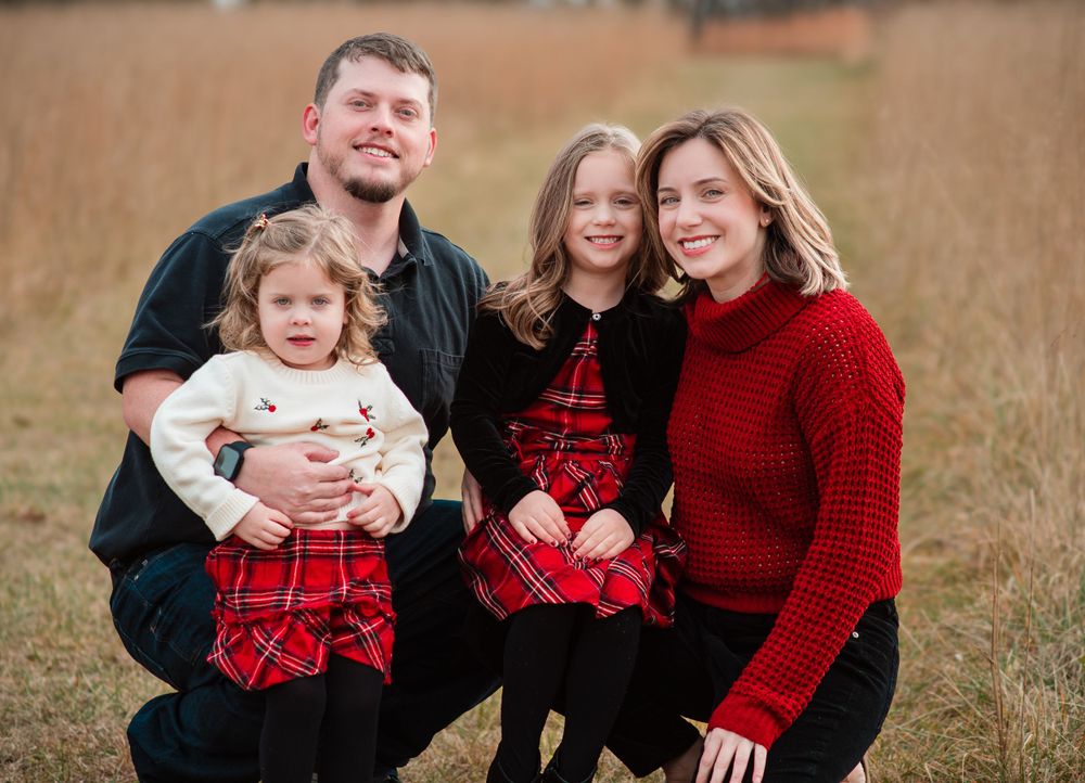Family of four wearing red and black coordinated outfits poses in autumn field.