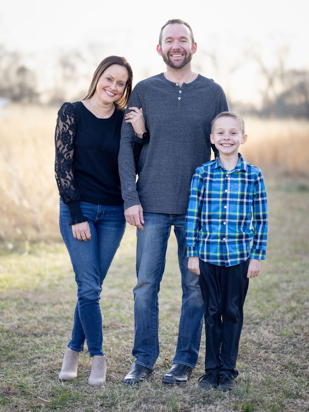 A group of three poses together outdoors with tall grass and trees in the background.