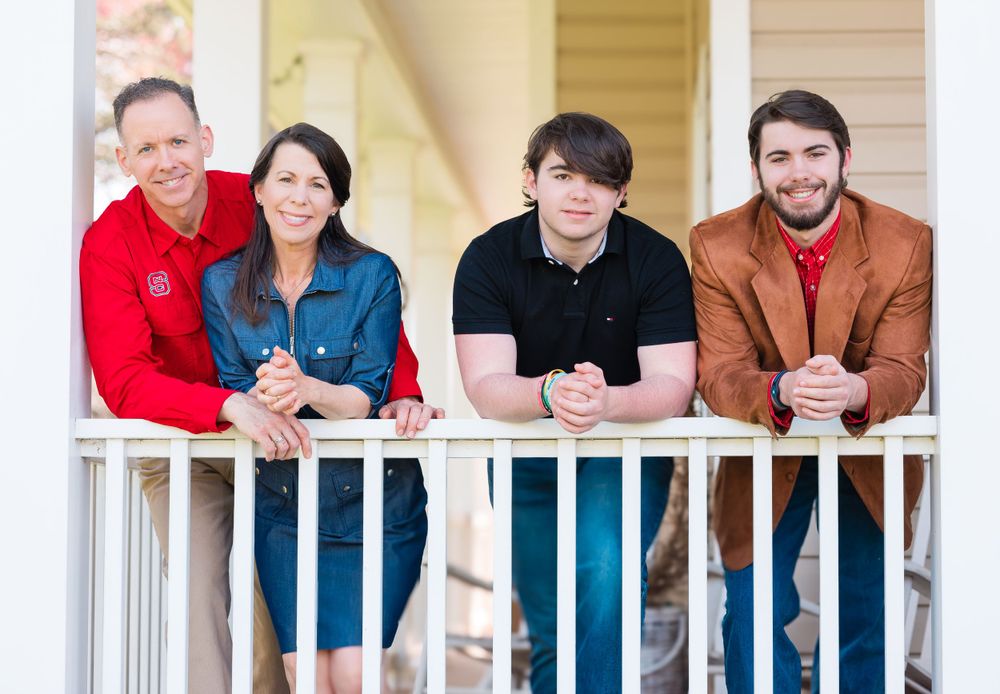 Group portrait of four people sitting together on white porch railing.