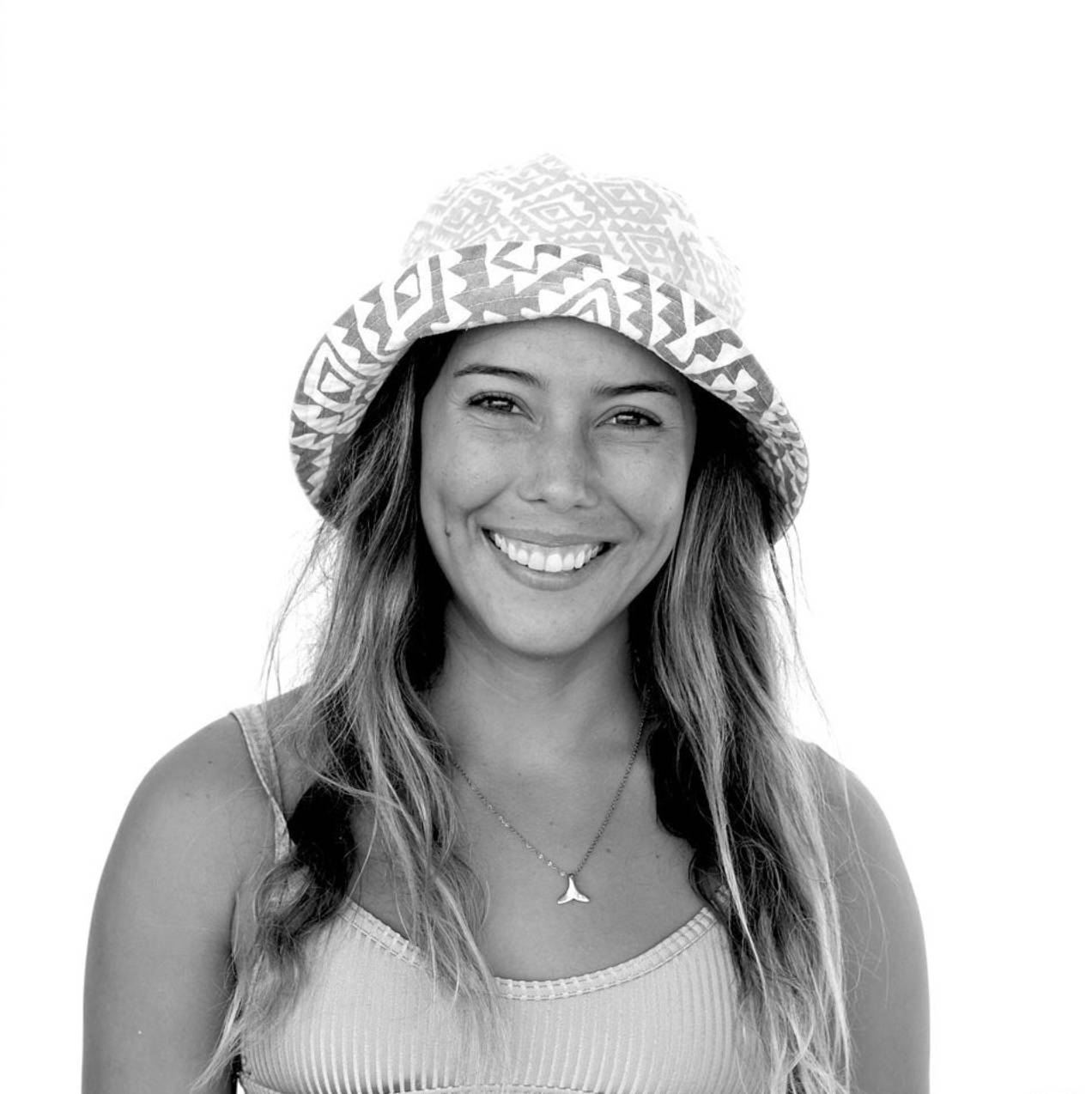 Black and white portrait of someone in a knit bucket hat and tank top, smiling brightly at the camera.