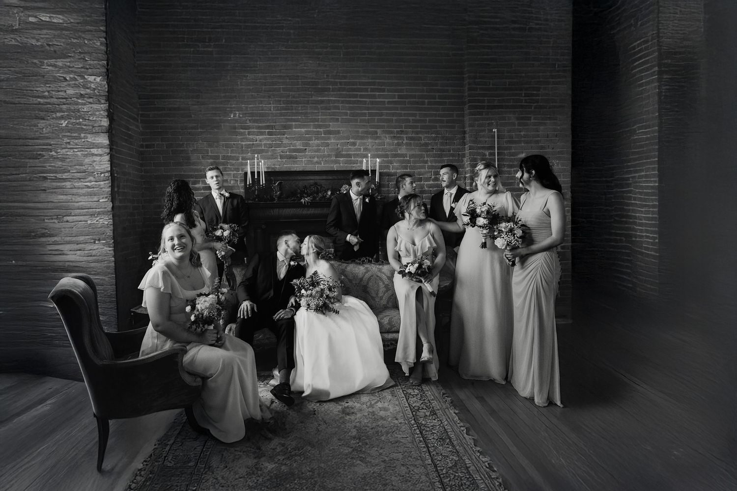 Wedding party gathered in elegant black and white photograph with moody lighting and brick backdrop. Pittsburgh Weddings