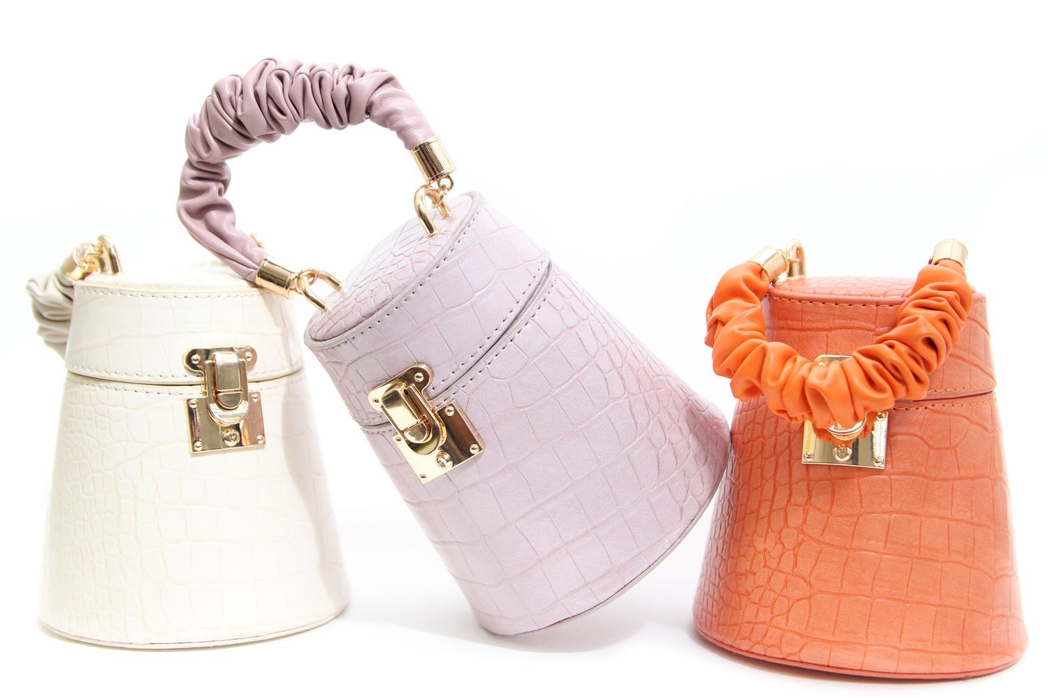 Three small purses with scrunchie handles in white, lilac, and orange colors arranged in a row with gold metal clasps.