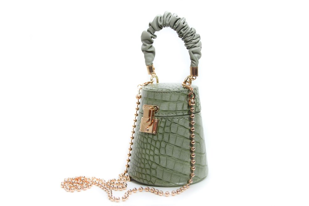 Mint green crocodile-textured mini handbag with braided handle and gold chain strap on white background.