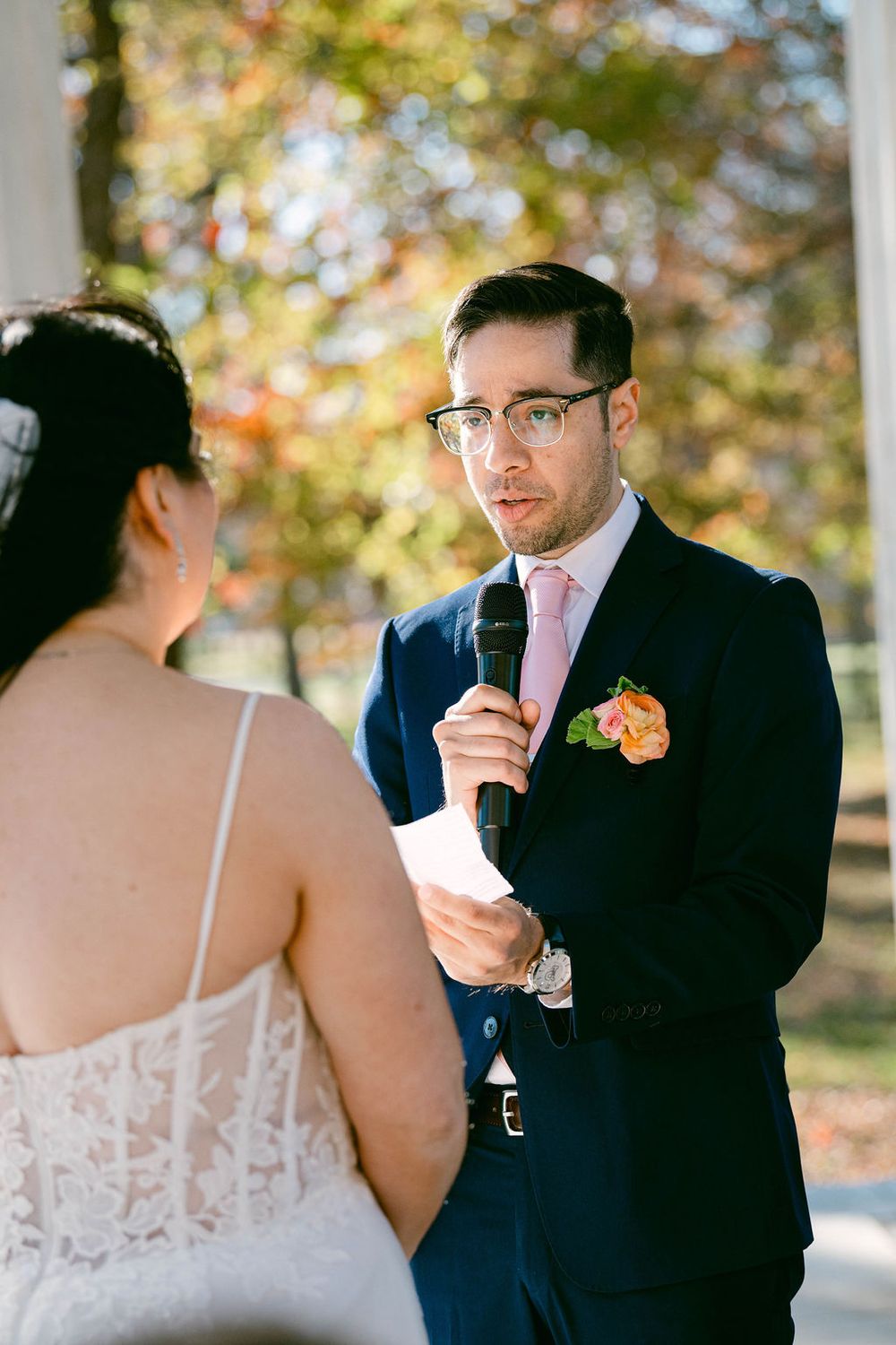 A couple shares an emotional moment during their outdoor autumn wedding ceremony with fall foliage in the background.