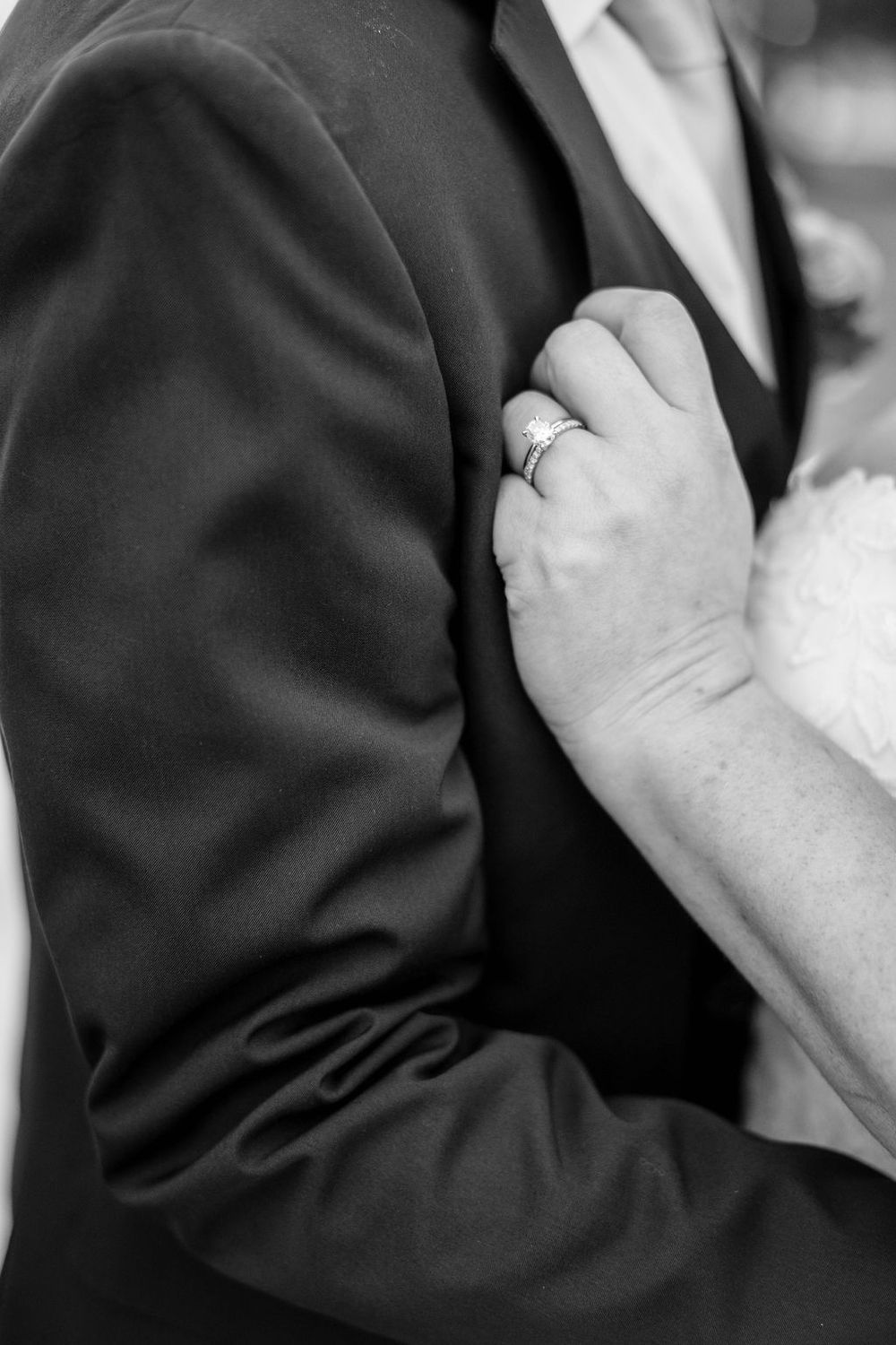 Close-up black and white detail of hands with wedding rings in formal attire.