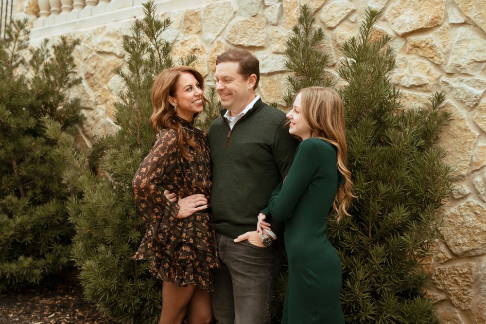 A group poses outdoors against a stone wall backdrop in coordinated green and brown autumn outfits.