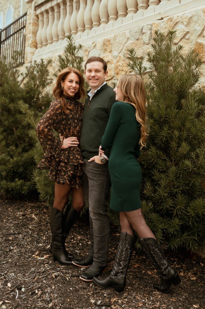 Family group posing together against a stone wall with evergreen bushes.