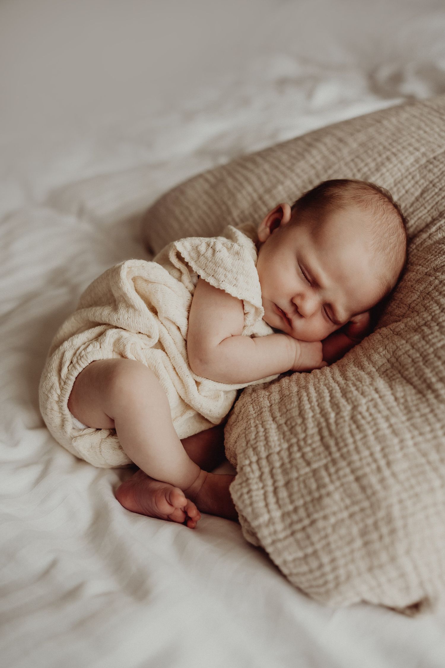 A sleeping newborn baby lies peacefully on white bedding in a series of connected photographs.