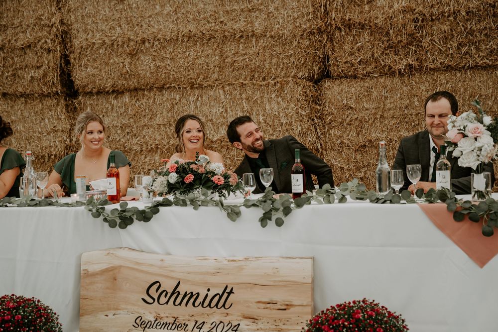 wedding reception head table. groom laughs as bride looks on during speeches