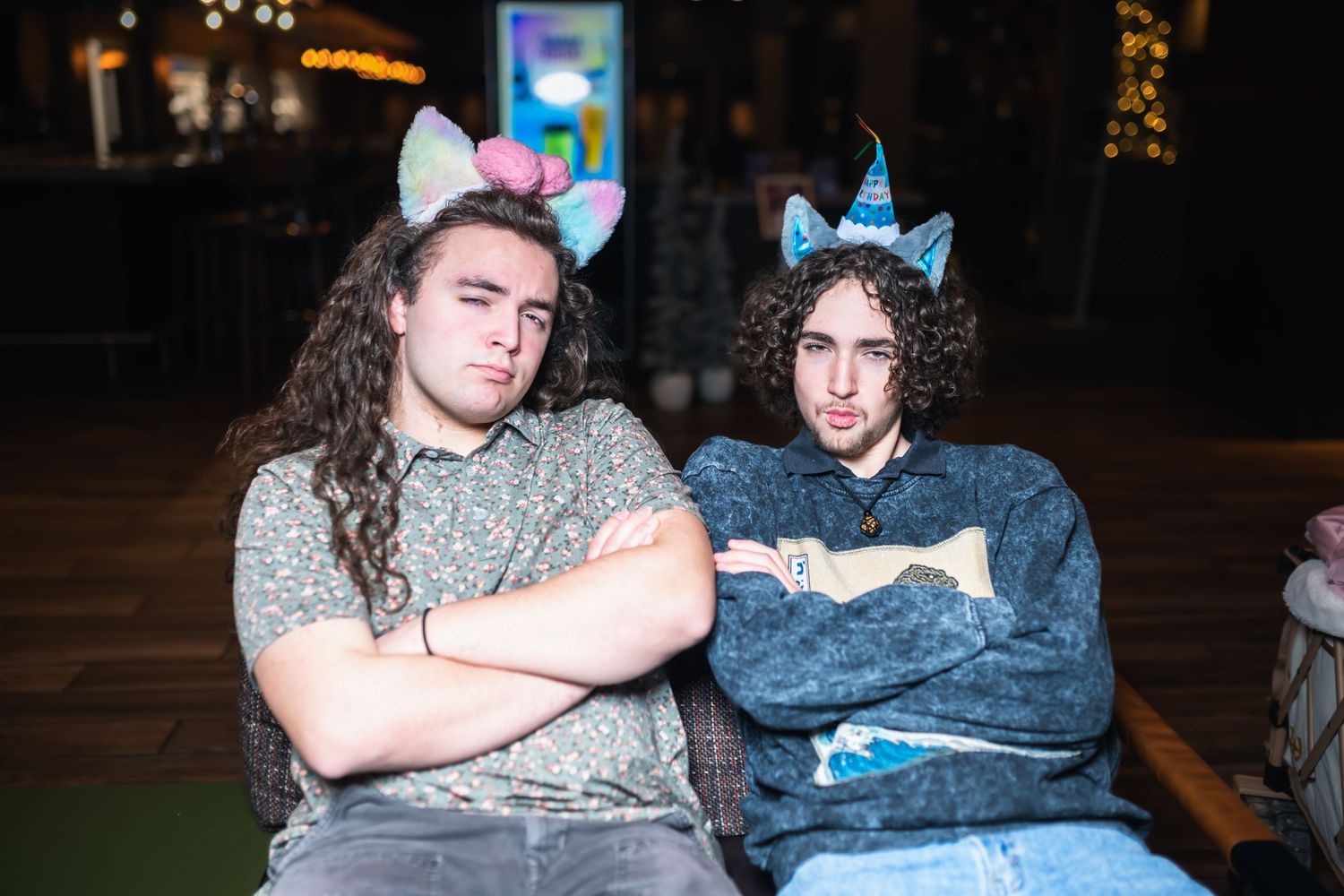 Two people in party hats sit close together on a couch during a celebration.