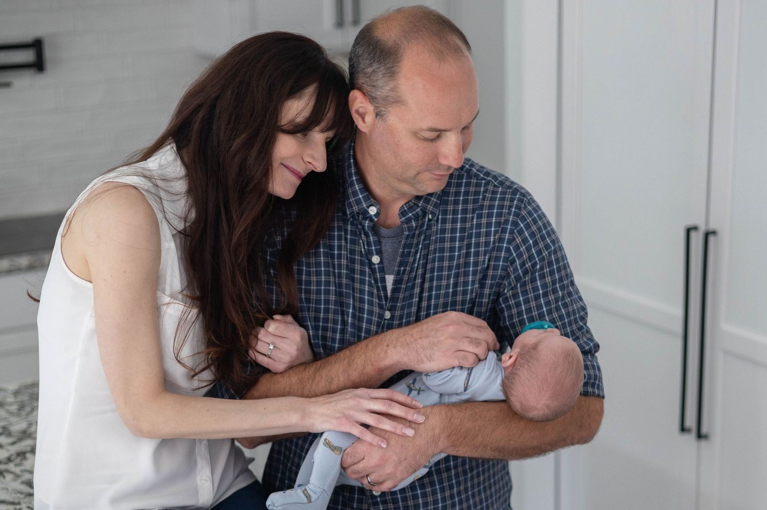 A Pinehurst couple lovingly gazes at their newborn baby in a bright, modern kitchen setting.