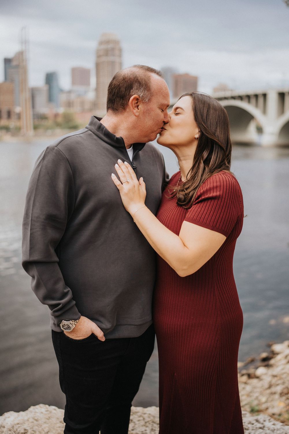 A couple shares intimate moments by the waterfront with a city skyline backdrop in a romantic photoshoot series.