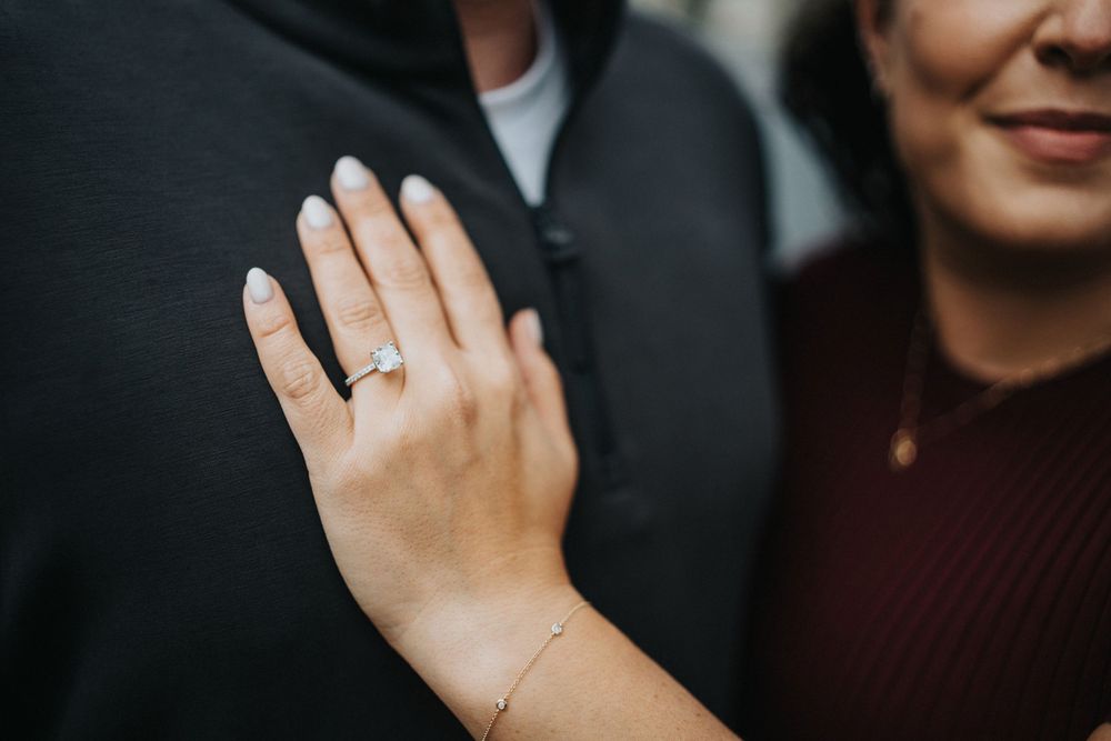 Close up view of hands showing off sparkling engagement rings and wedding bands against dark background.