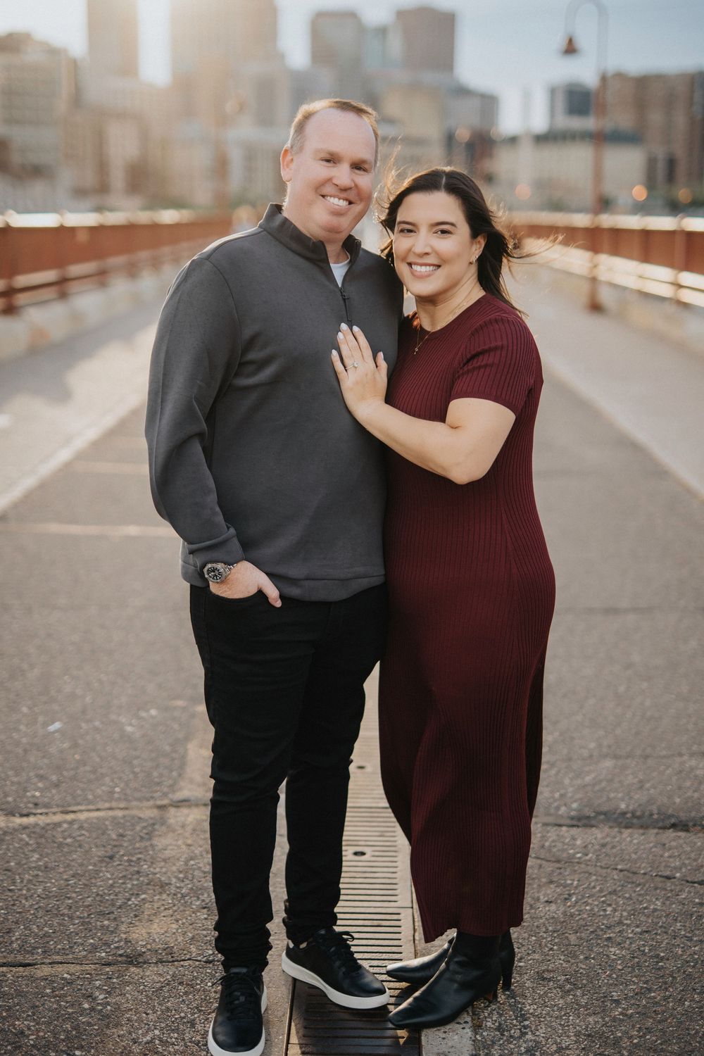 A couple shares joyful moments during a photoshoot on a rooftop walkway with urban skyline views.