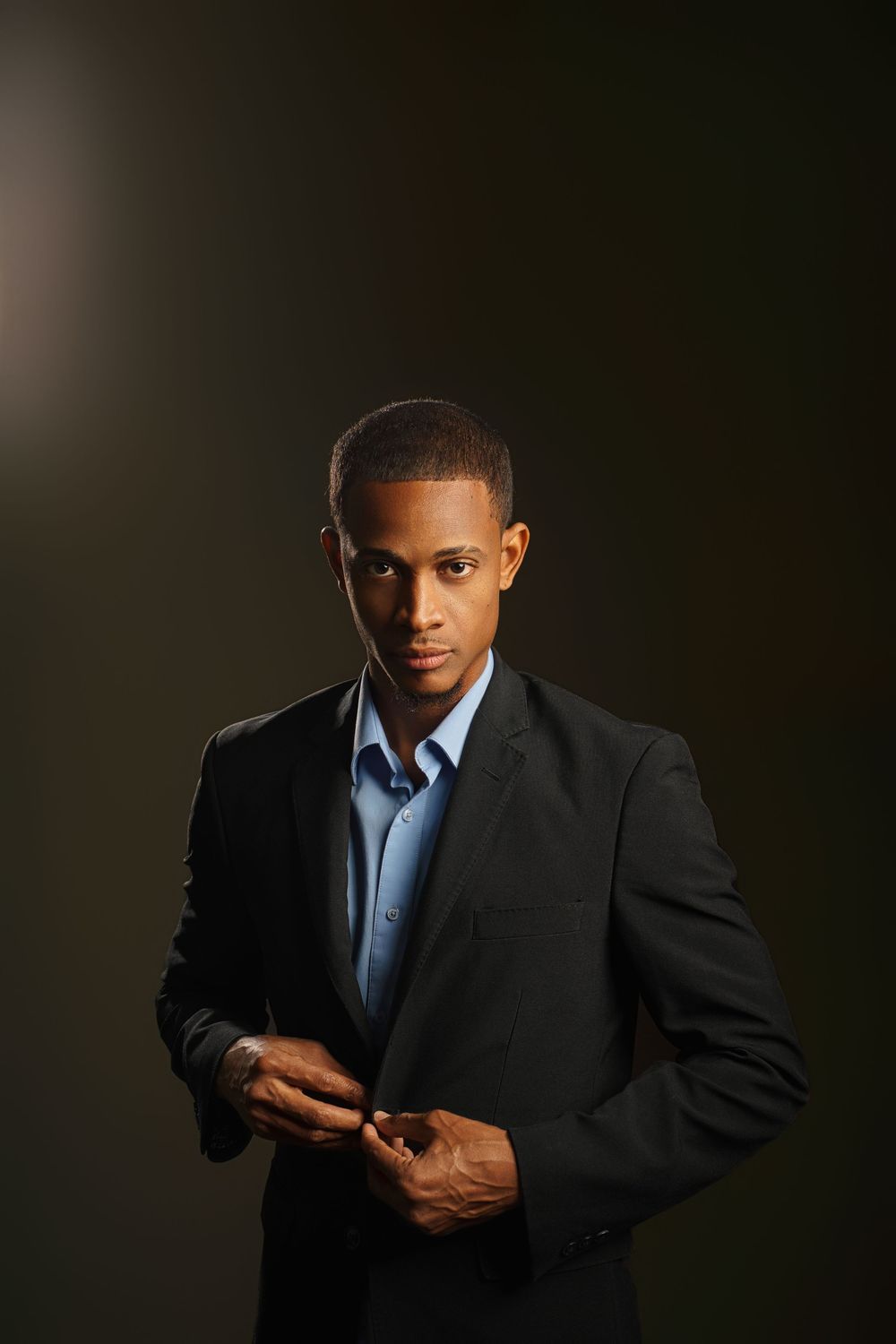 Professional portrait series showing a man in a dark suit and blue tie checking his phone in dramatic lighting.