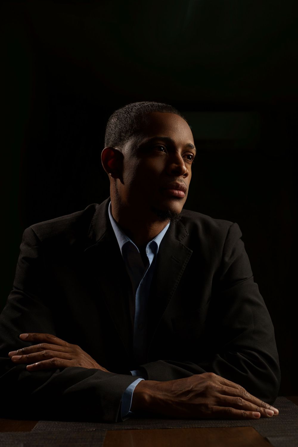 A series of dramatic low-key portraits showing a person in a dark suit sitting at a table against a black background.
