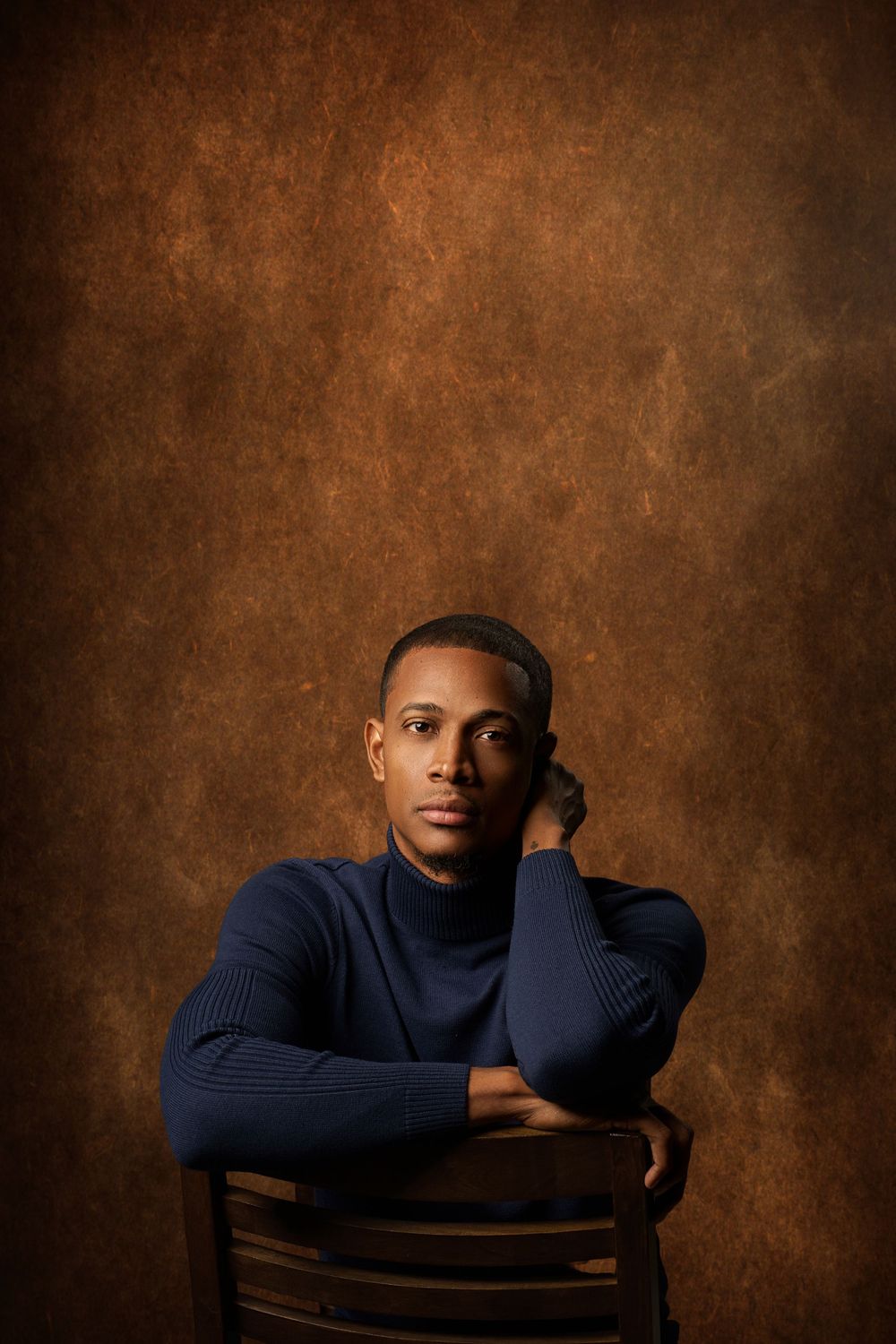 Professional studio portraits in warm brown tones showing contemplative poses in navy turtleneck against textured backdrop.