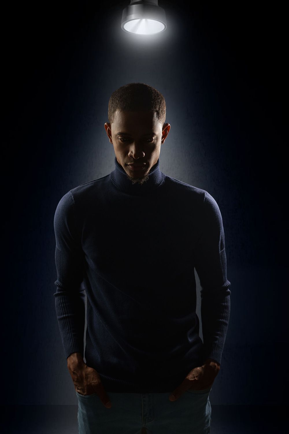 Dramatic silhouette of a figure in darkness illuminated by overhead spotlights creating an eerie atmospheric effect.