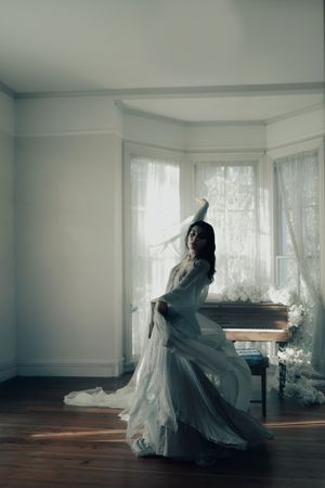 A dramatic silhouette of a flowing white dress twirling near a piano in a sunlit room with sheer curtains.