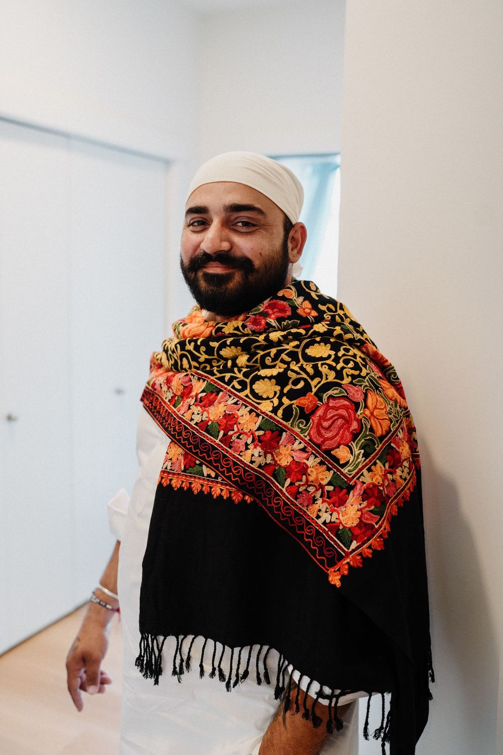 Smiling Sikh man wearing white turban and colorful floral embroidered black shawl.