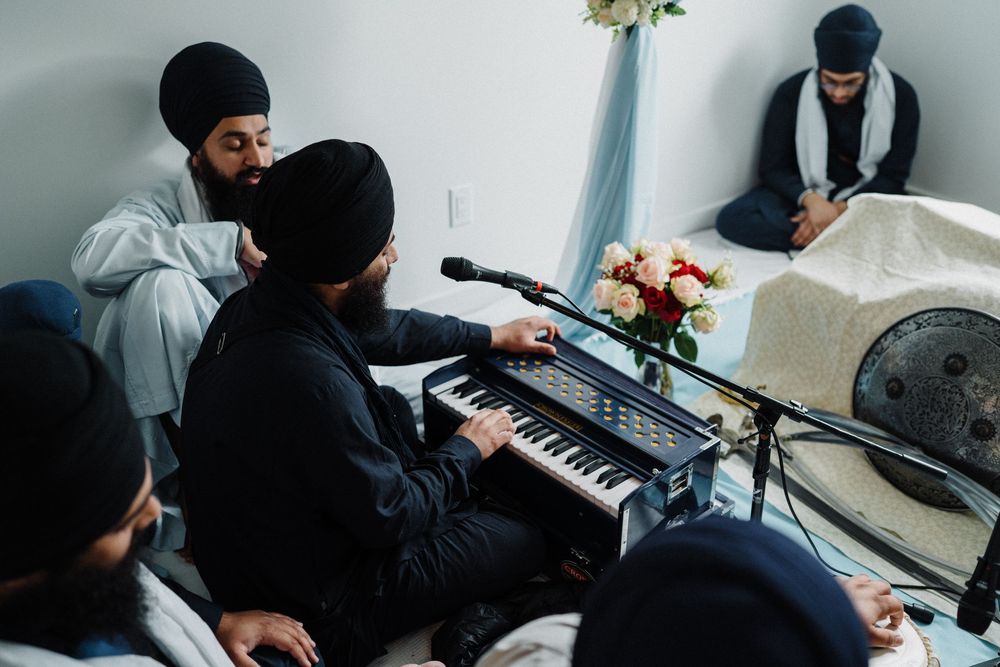 Sikh musicians playing harmonium during religious ceremony in decorated indoor setting.