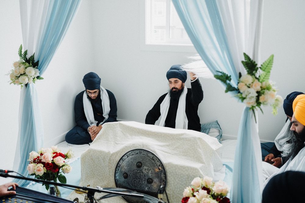 Sikh granthi performing chaur sahib ceremony over holy scripture at decorated altar.