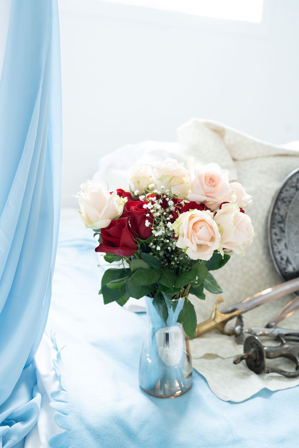 Bouquet of red and pink roses in glass vase on blue fabric beside ceremonial Sikh items.