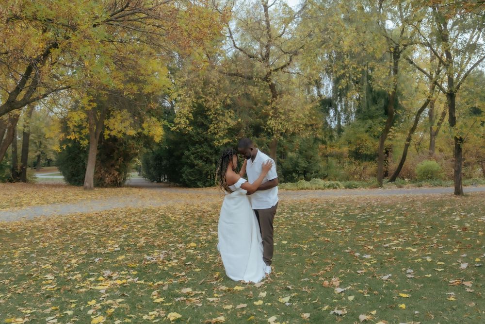 A couple shares a romantic moment in a park filled with golden autumn leaves and tall trees.