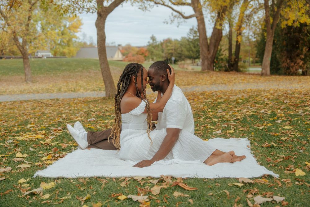 A couple shares an intimate moment on a white blanket surrounded by fallen autumn leaves in a park.