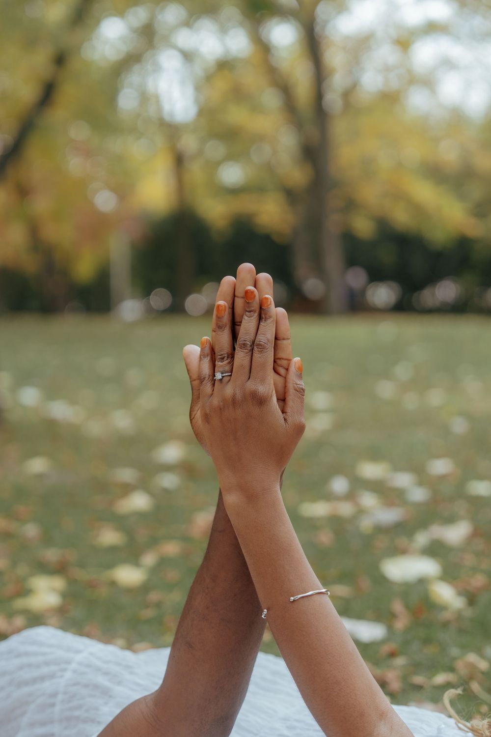 Two hands raised together against a blurred autumn background with fallen leaves.