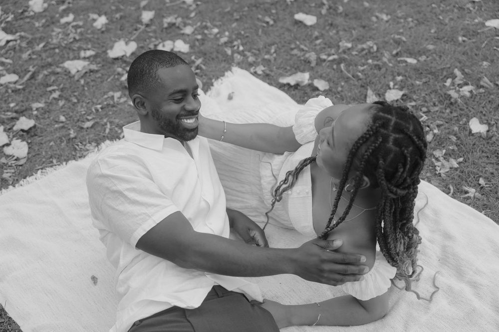 A couple shares an intimate moment lying on a white blanket outdoors.