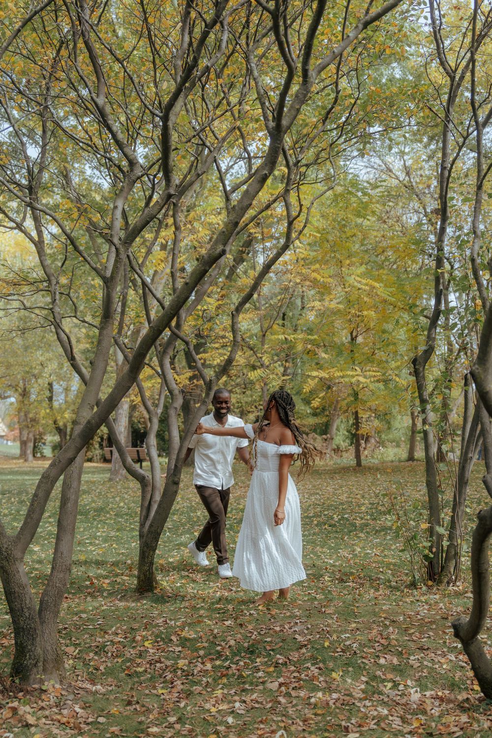 A romantic moment unfolds between two people dancing among fall foliage in a wooded area.