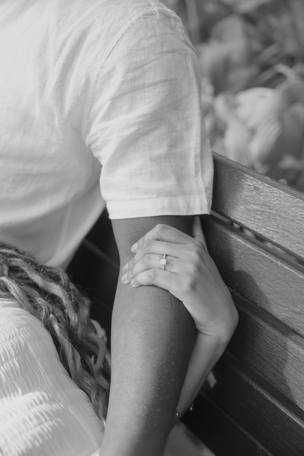 Close-up detail of white linen clothing and hands resting on a wooden surface.