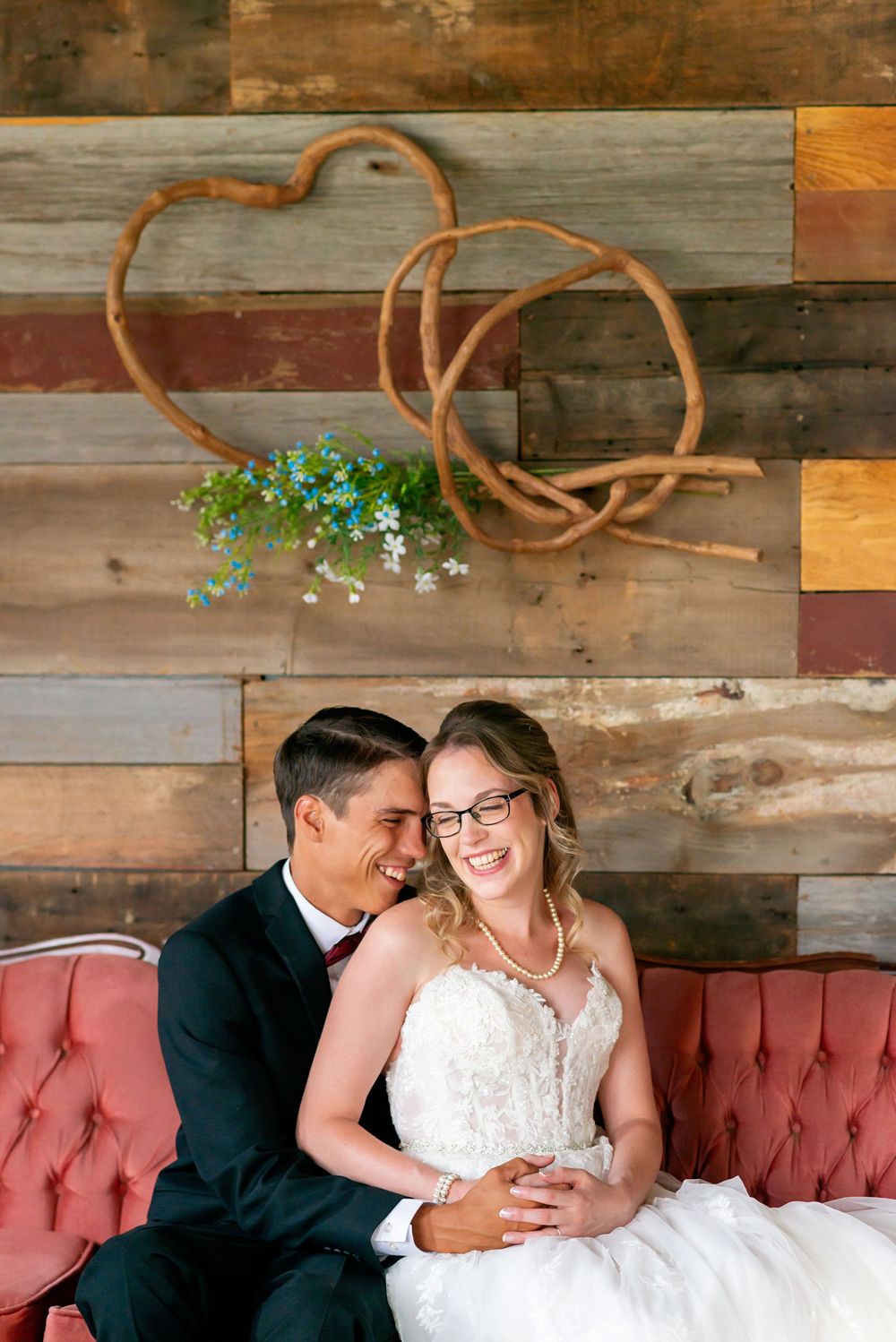 Intimate moments captured on vintage red couch against reclaimed wood wall background at Pondvalley Manor.