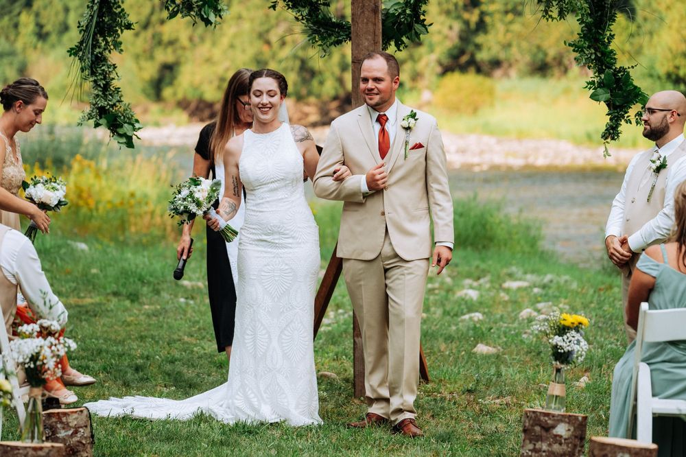 A wedding ceremony in a lush outdoor setting with the couple walking down a grassy aisle surrounded by guests.