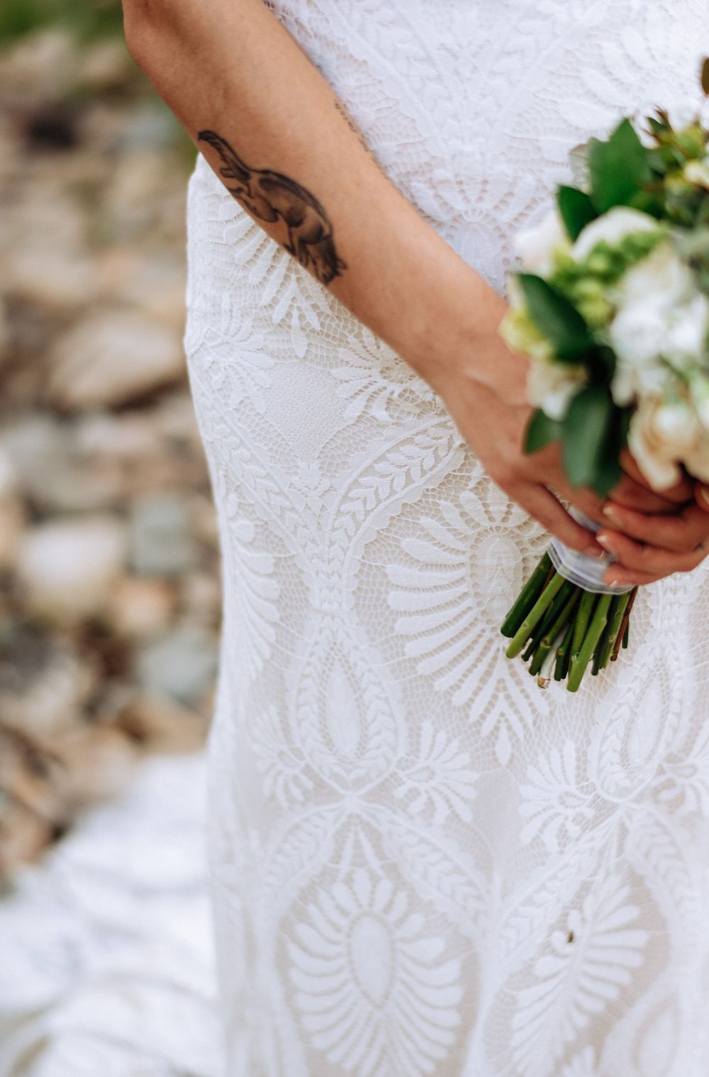 Close-up details of an elegant white lace wedding dress with intricate patterns and a bridal bouquet.