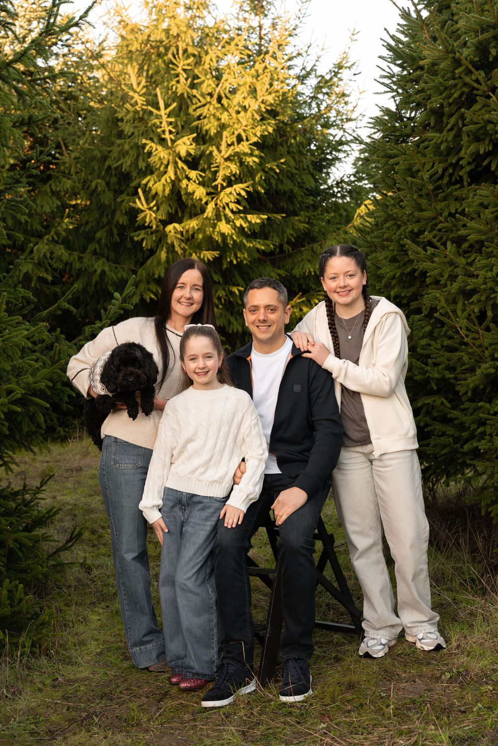 A group wearing coordinated cream and gray outfits poses together against evergreen trees in an outdoor setting.