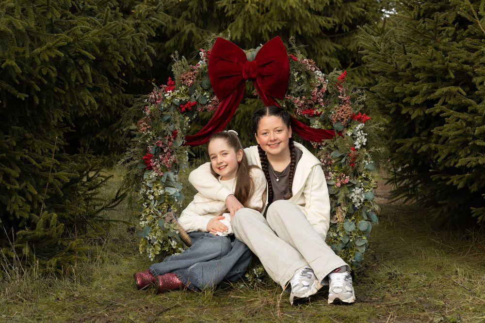 A group of people pose together in a garden setting with red flowers and greenery in the background.