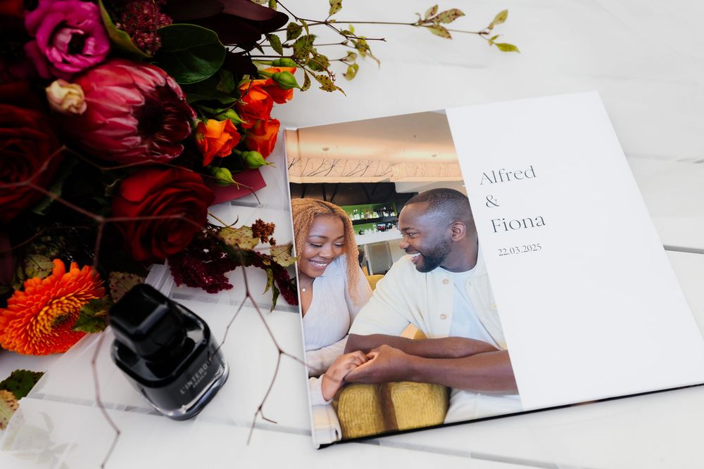 Wedding place cards and elegant floral arrangements with burgundy roses and greenery on a white surface.