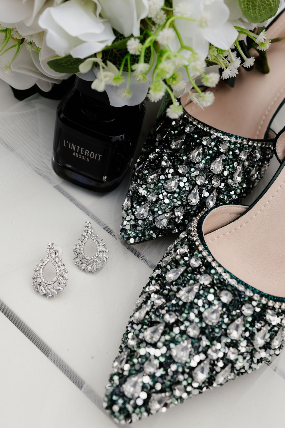 Elegant bridal accessories including sparkly shoes and jewelry arranged with white flowers against a light background.